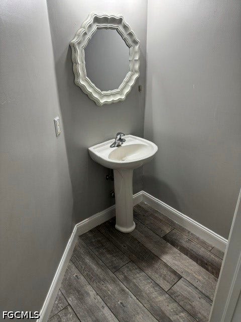 Pedestal sink with chrome faucet, decorative framed mirror, and wood-finish flooring