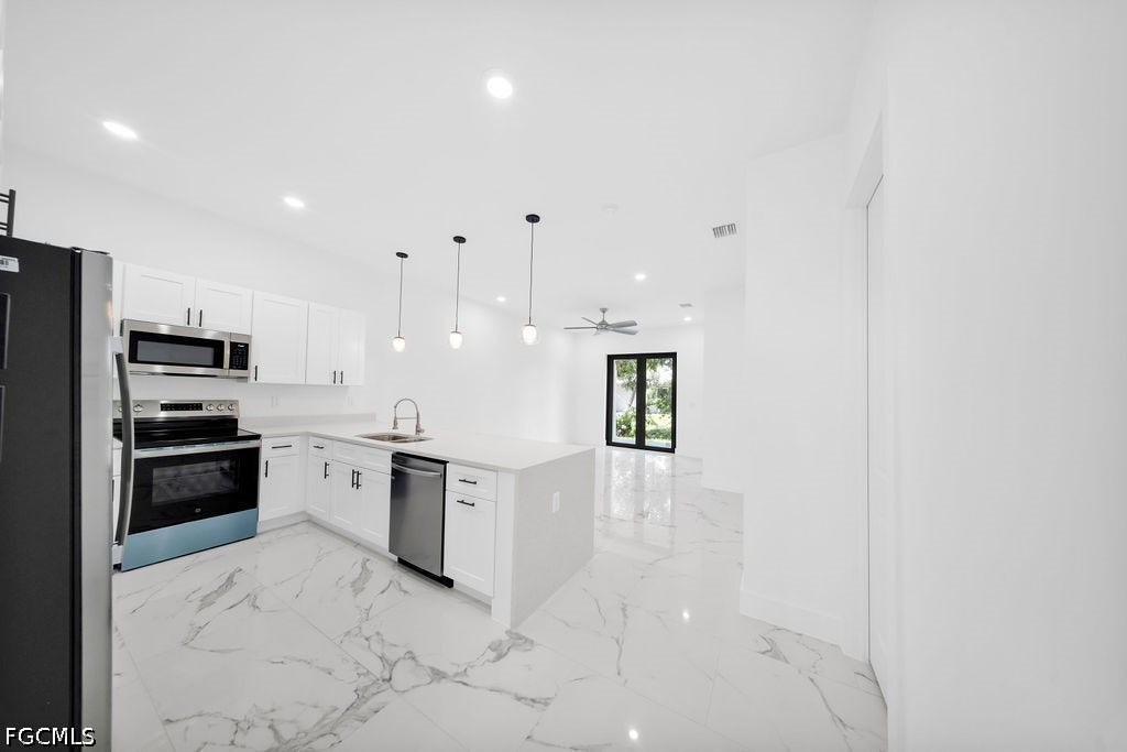 2416/2418 Joe Avenue S, Lehigh Acres, FL 33973 Kitchen featuring white cabinetry, stainless steel appliances, a center island with sink, and pendant lighting
