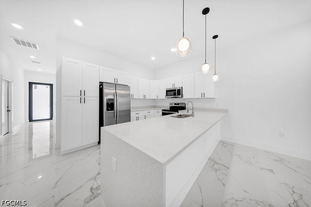 2416/2418 Joe Avenue S, Lehigh Acres, FL 33973 Modern kitchen featuring a central island with an integrated sink, white shaker cabinetry, stainless steel appliances, and pendant lighting
