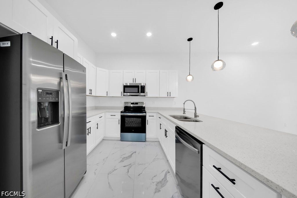 2416/2418 Joe Avenue S, Lehigh Acres, FL 33973 U-shaped kitchen with white cabinetry and black hardware, stainless steel appliances, light-toned countertops, and pendant lighting