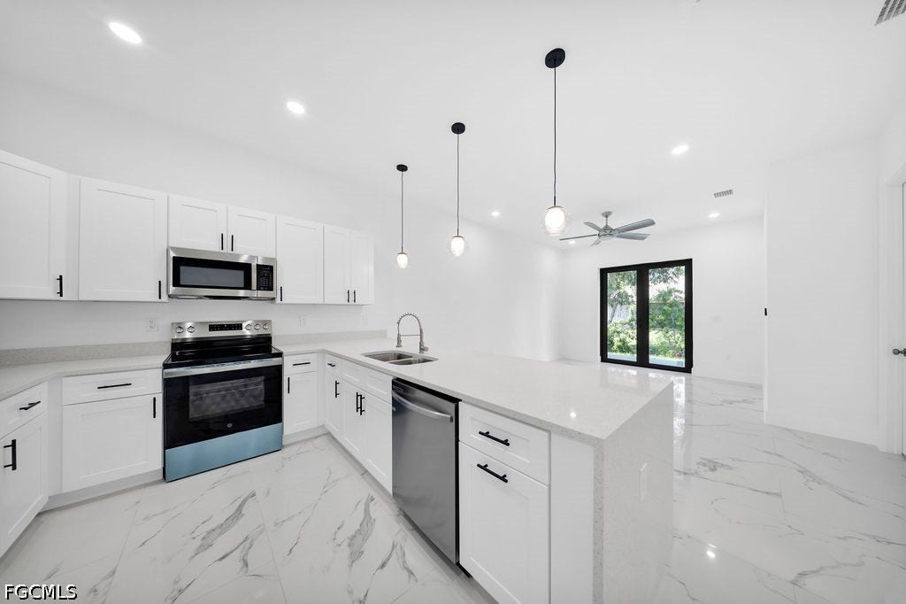 2416/2418 Joe Avenue S, Lehigh Acres, FL 33973 Sleek kitchen with white cabinetry, stainless steel appliances, and a central island with a sink