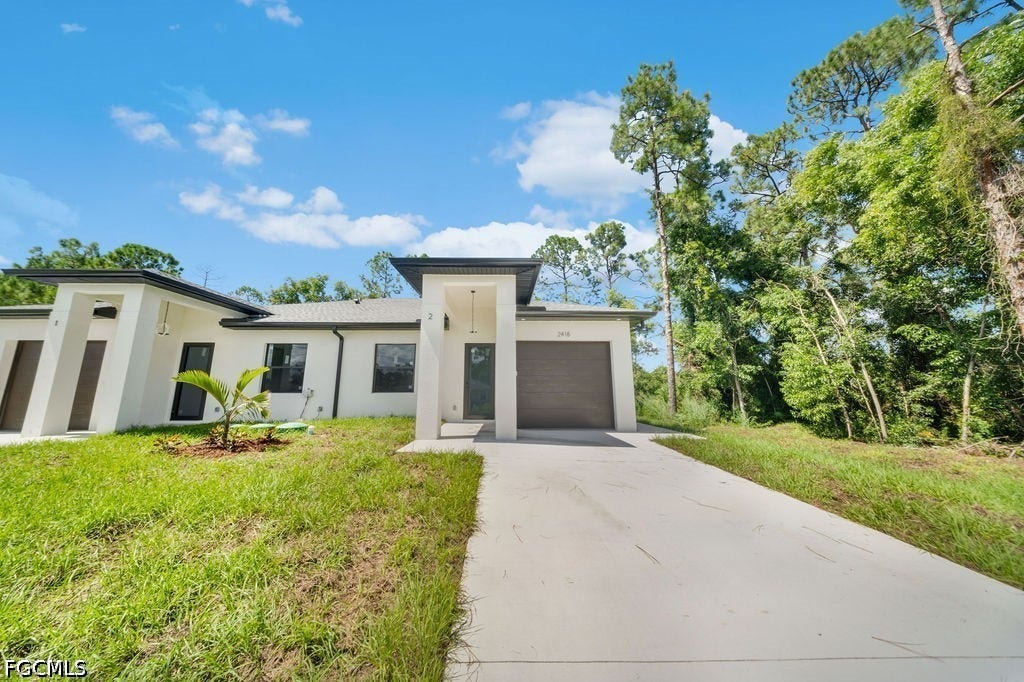 2416/2418 Joe Avenue S, Lehigh Acres, FL 33973 Modern exterior architecture with a gray garage door, concrete driveway, and a well-maintained lawn