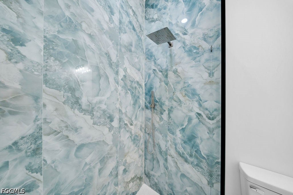 2416/2418 Joe Avenue S, Lehigh Acres, FL 33973 Shower featuring blue-toned marbled wall tile, a square rain shower head, and a handheld shower fixture