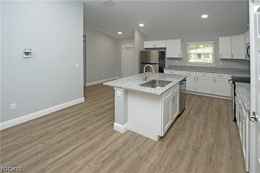 9342/9344 N Peachtree Way, Citrus Springs, FL 34434 Kitchen featuring an island with an undermount sink, stainless steel appliances, white cabinetry, speckled countertops, and wood-finish flooring