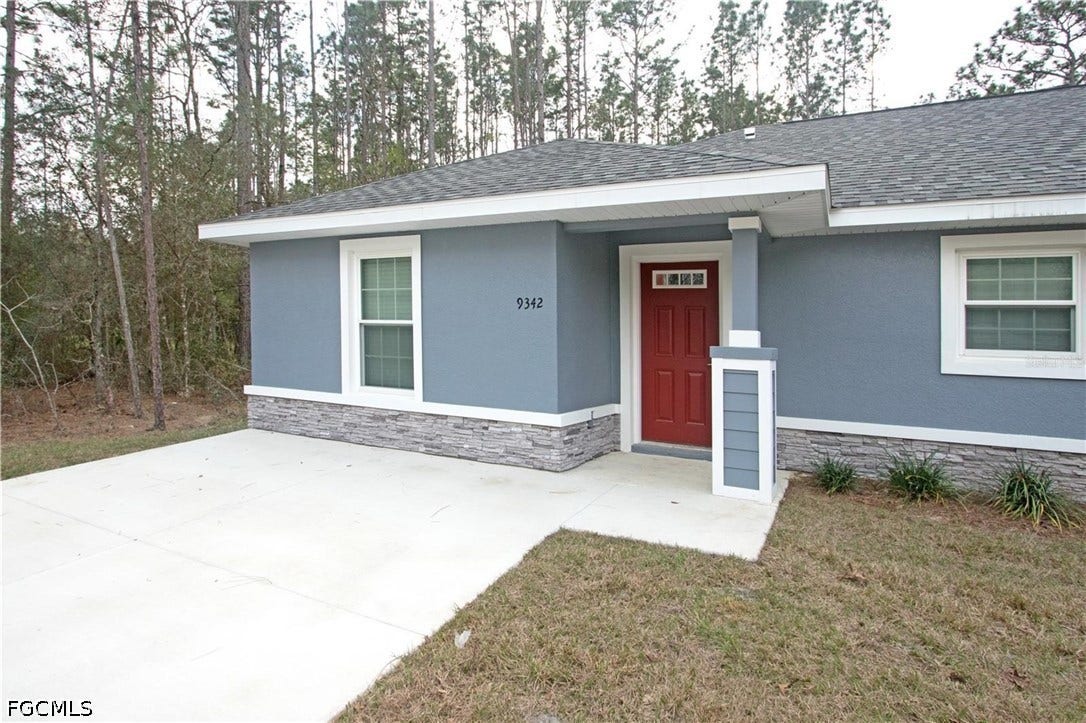 9342/9344 N Peachtree Way, Citrus Springs, FL 34434 Stucco exterior with stone-look accent siding, red entry door with transom window, white trim, and a gray shingle roof