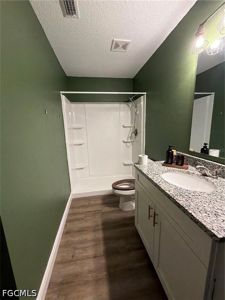 9342/9344 N Peachtree Way, Citrus Springs, FL 34434 Bathroom featuring wood-finish flooring, a white vanity with a speckled countertop, an integrated sink, and a shower with built-in shelving
