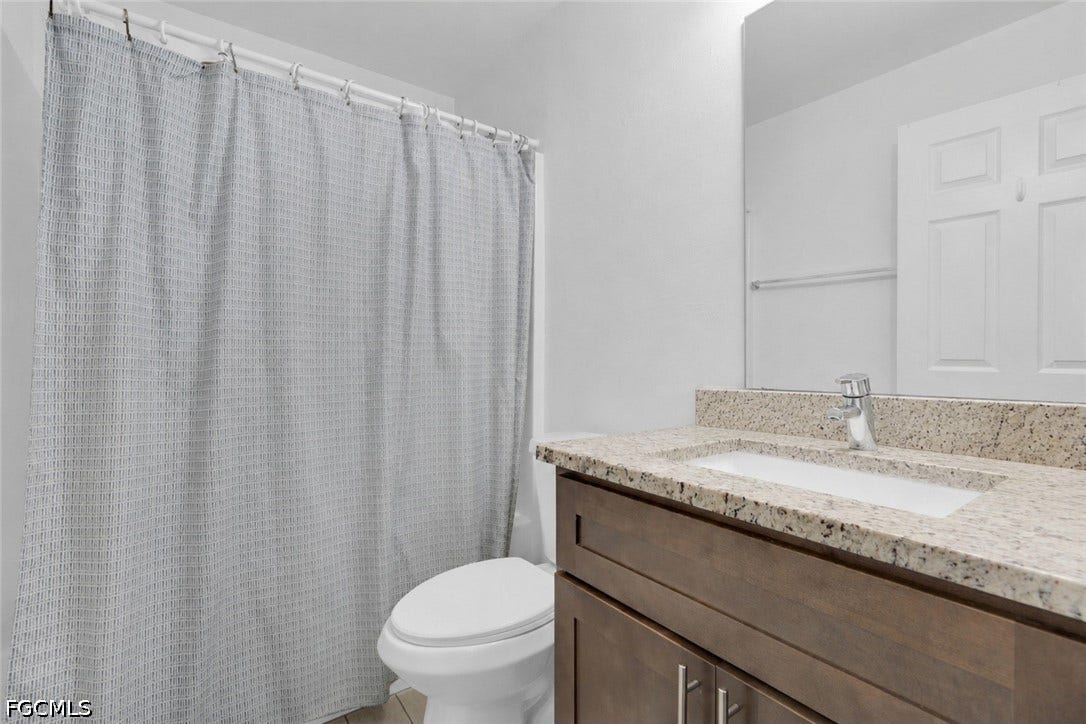 2412/2414 Richard Avenue S, Lehigh Acres, FL 33973 Granite-style countertop with an integrated sink, wood-finish vanity, and a wall-mounted mirror