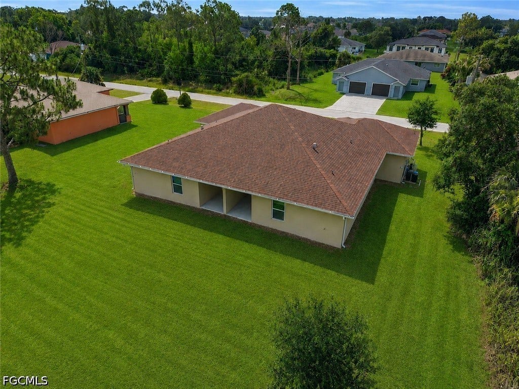 2412/2414 Richard Avenue S, Lehigh Acres, FL 33973 Expansive green lawn surrounds a single-story structure with a brown shingle roof, light-colored exterior, and an integrated covered patio area