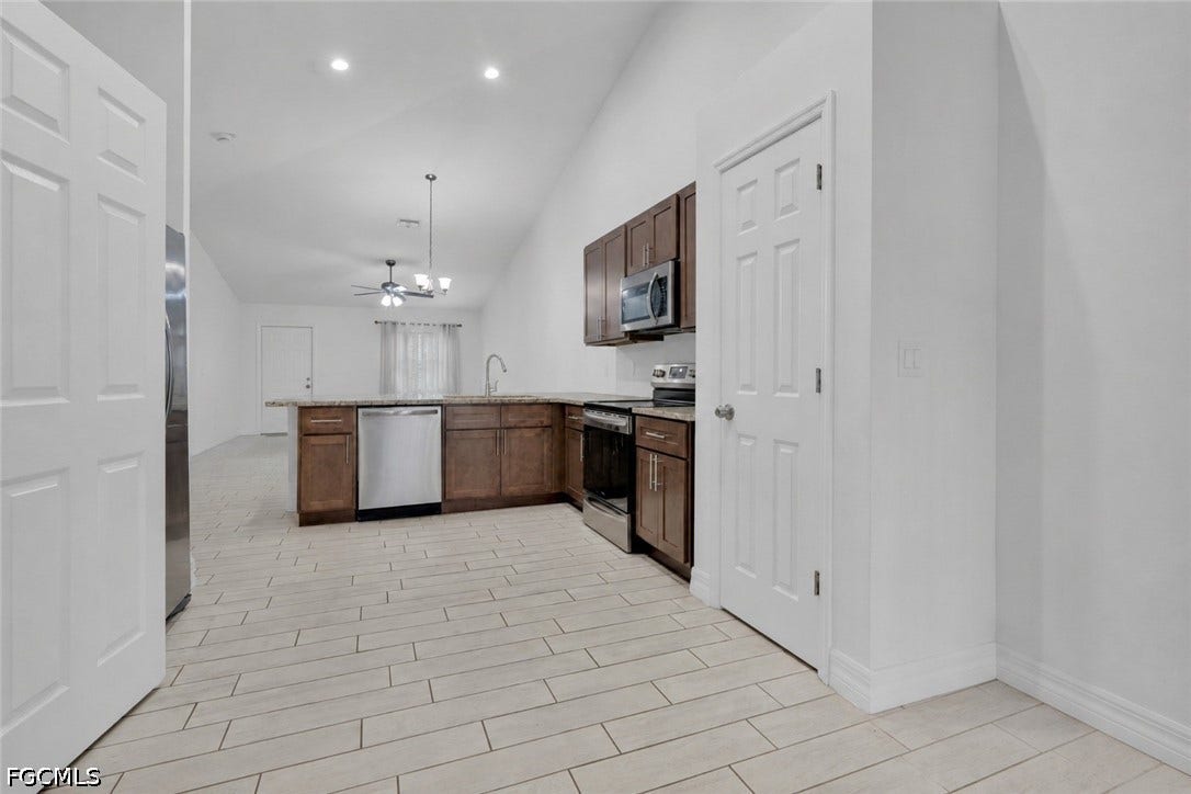 2412/2414 Richard Avenue S, Lehigh Acres, FL 33973 Kitchen featuring wood-finish cabinetry, stainless steel appliances, and a peninsula with a stone-finish countertop