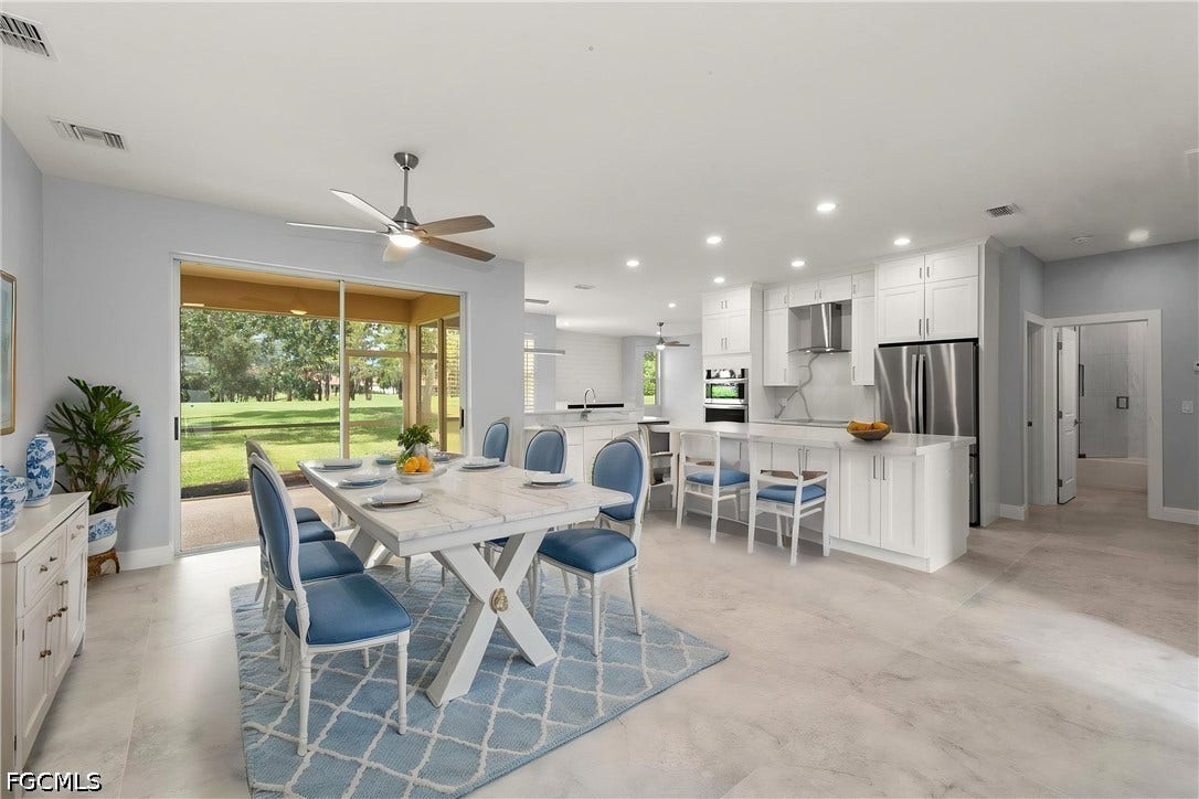 Spacious open-concept living area featuring light-toned flooring, white shaker cabinetry, stainless steel appliances, and a screened patio with green landscaping