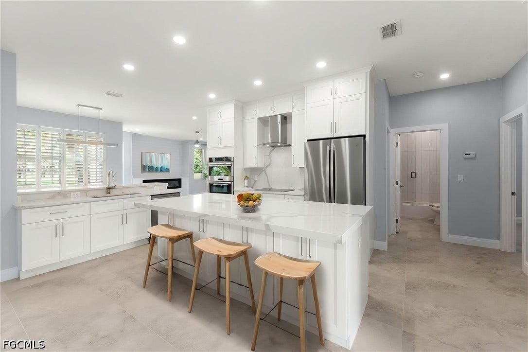White cabinetry, stainless steel appliances, recessed lighting, a kitchen island with seating, and light-toned flooring