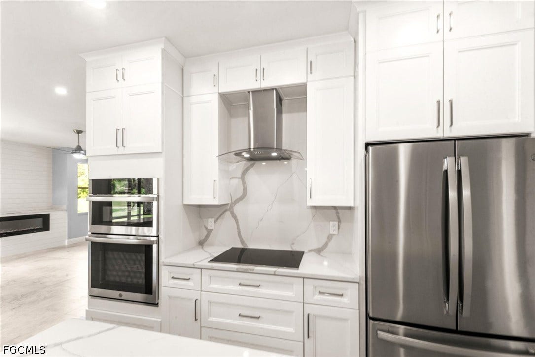 White shaker cabinetry complemented by a waterfall countertop, stainless steel appliances, a built-in wall oven, and a modern range hood