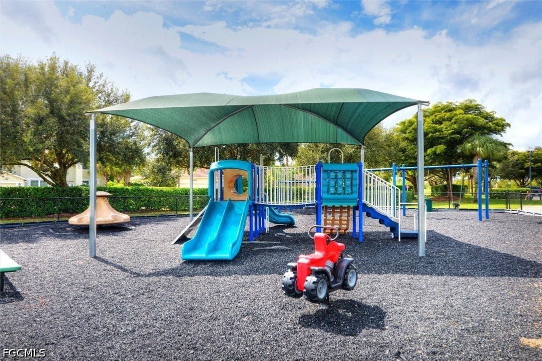 Playground area featuring a shade canopy, rubberized ground surfacing, slide, climbing structure, and spring rider