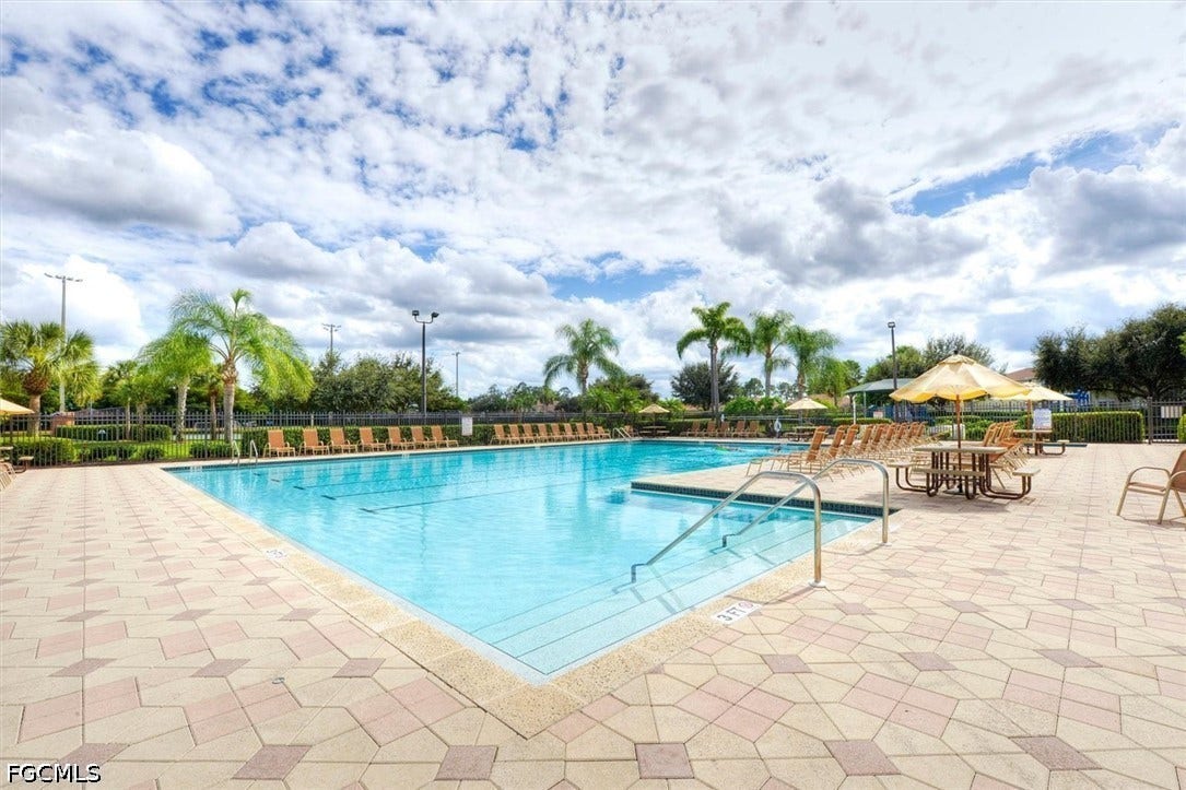 Expansive outdoor pool with integrated steps, surrounded by patterned paver decking, multiple lounging chairs, and mature palm trees
