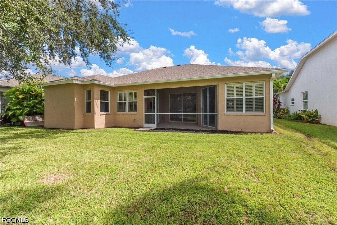 Spacious backyard with a screened lanai, stucco exterior, multiple windows with white shutters, and a well-maintained lawn
