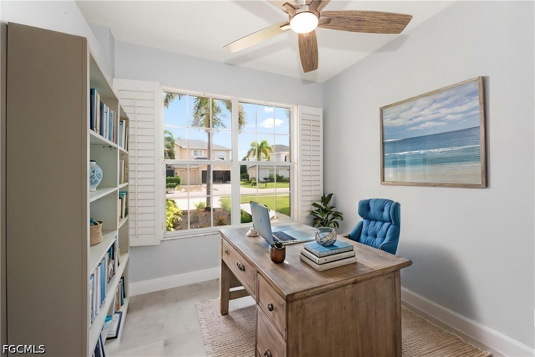 Built-in shelving, expansive window with plantation shutters, wood-finish ceiling fan, and light gray wall paint