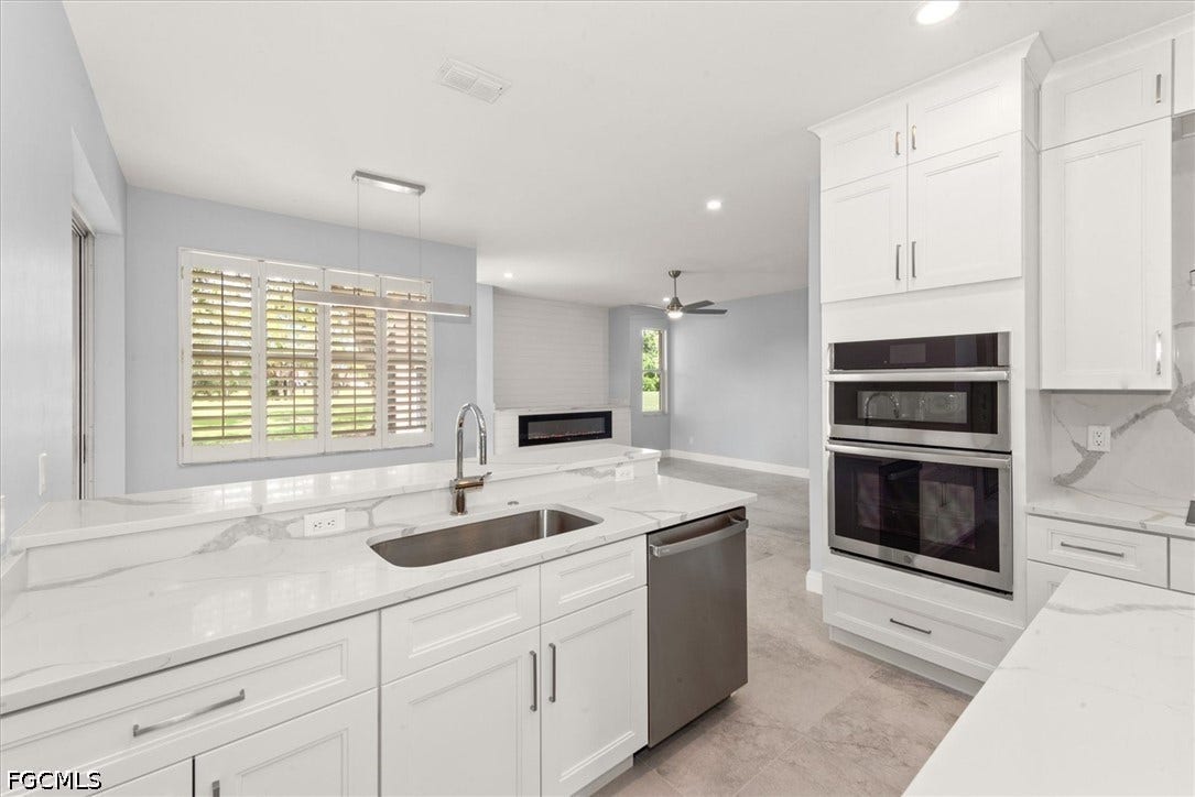 Kitchen featuring white cabinetry, light-toned countertops, stainless steel appliances, a built-in sink with a gooseneck faucet, and a linear pendant light fixture