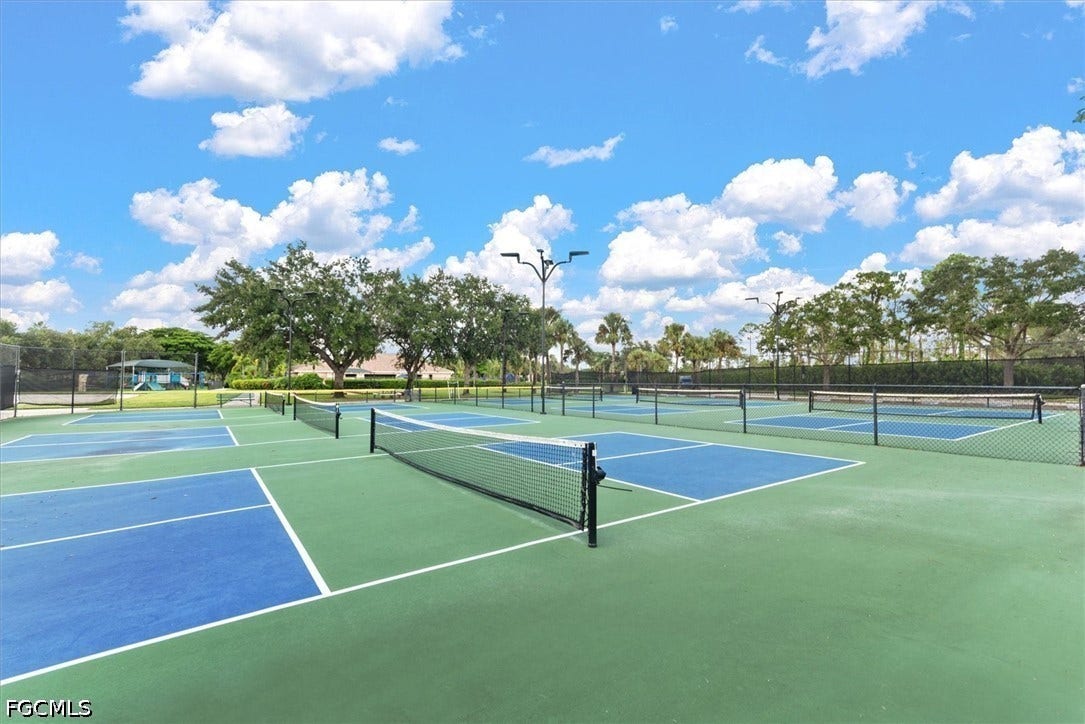 Multiple outdoor courts with blue and green surfacing, featuring black netting and perimeter fencing