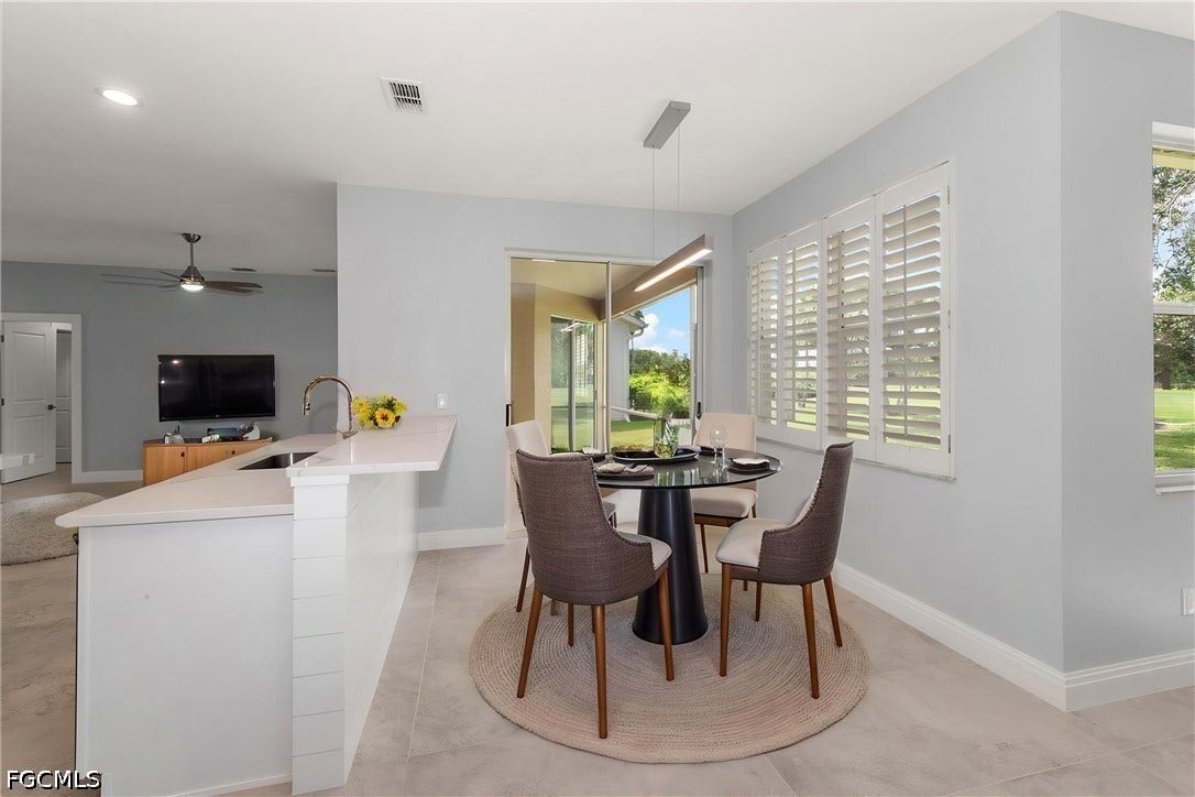Kitchen island with a built-in sink and white countertop, light tile flooring, white plantation shutters, and a sliding glass door