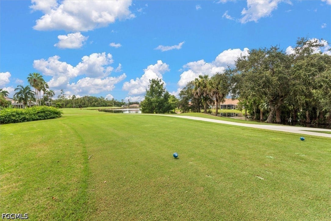 Expansive green space with distant water feature, mature trees, and a paved pathway