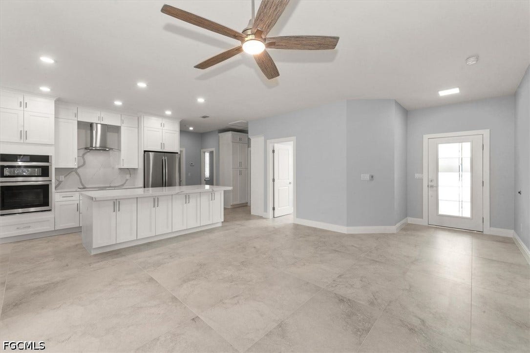 Open-concept kitchen and living area featuring a large center island, built-in stainless steel appliances, and light-toned tile flooring