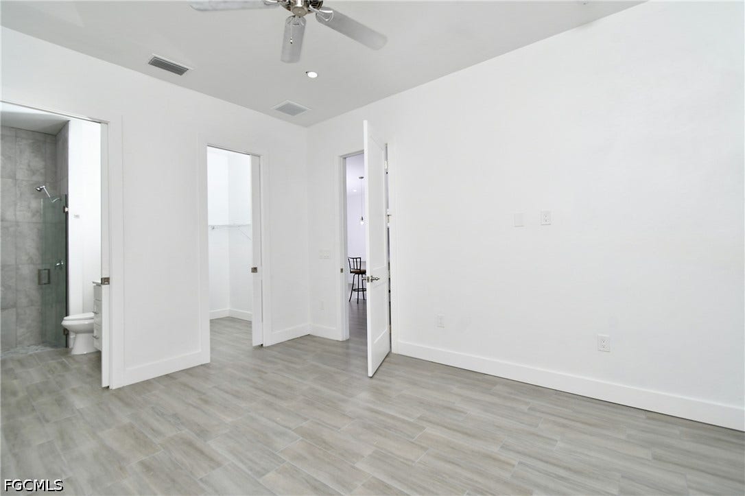 Unfurnished bedroom featuring a spacious closet, a ceiling fan, connected bathroom, and light wood finished floors