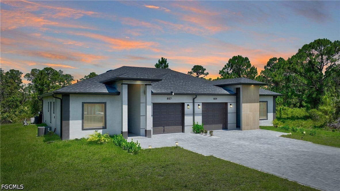 View of front of house featuring a yard, a garage, decorative driveway, and roof with shingles