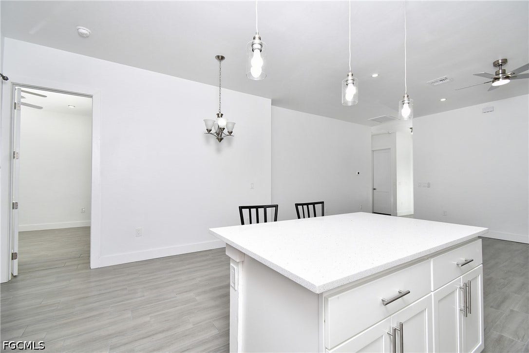 Kitchen with ceiling fan, white cabinets, and pendant lighting