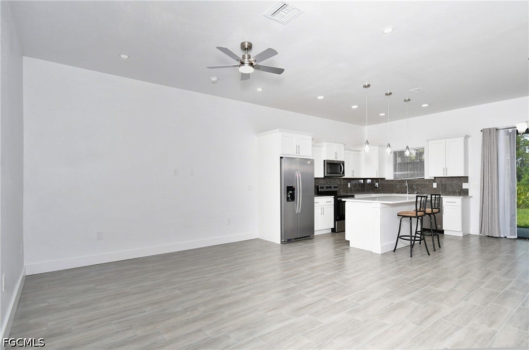 Kitchen featuring stainless steel appliances, open floor plan, hanging light fixtures, a breakfast bar, and a kitchen island