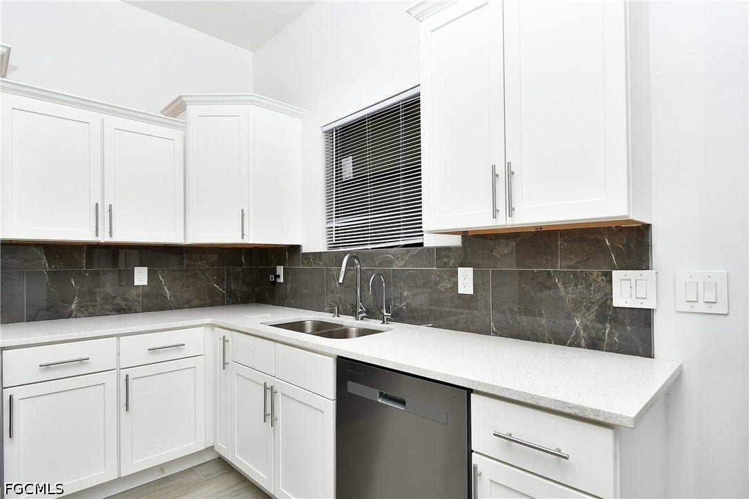 Kitchen featuring dishwasher, white cabinetry, light stone counters, and tasteful backsplash