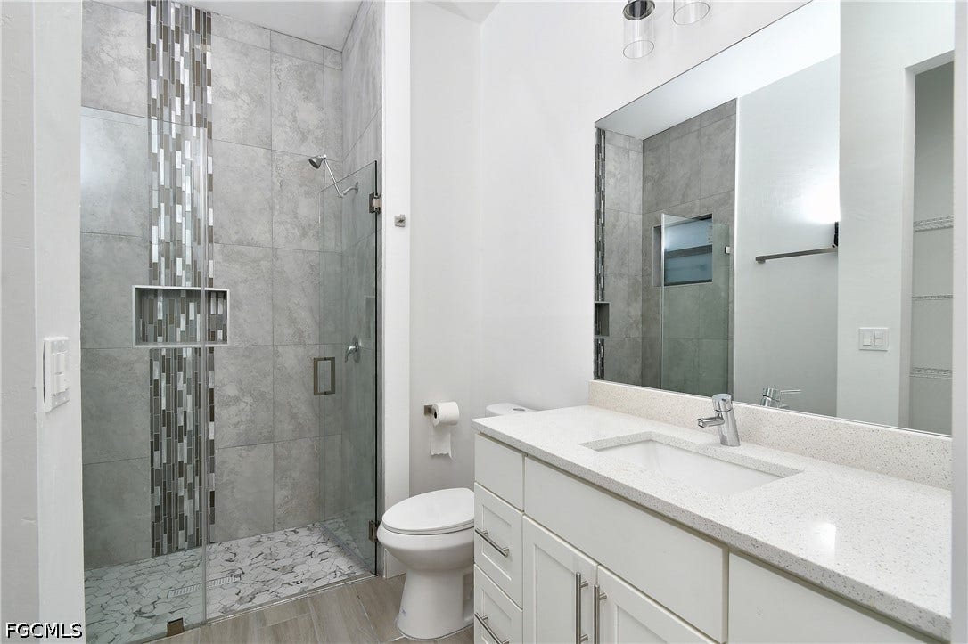 Bathroom with a shower stall, vanity, a walk in closet, and light wood-style flooring