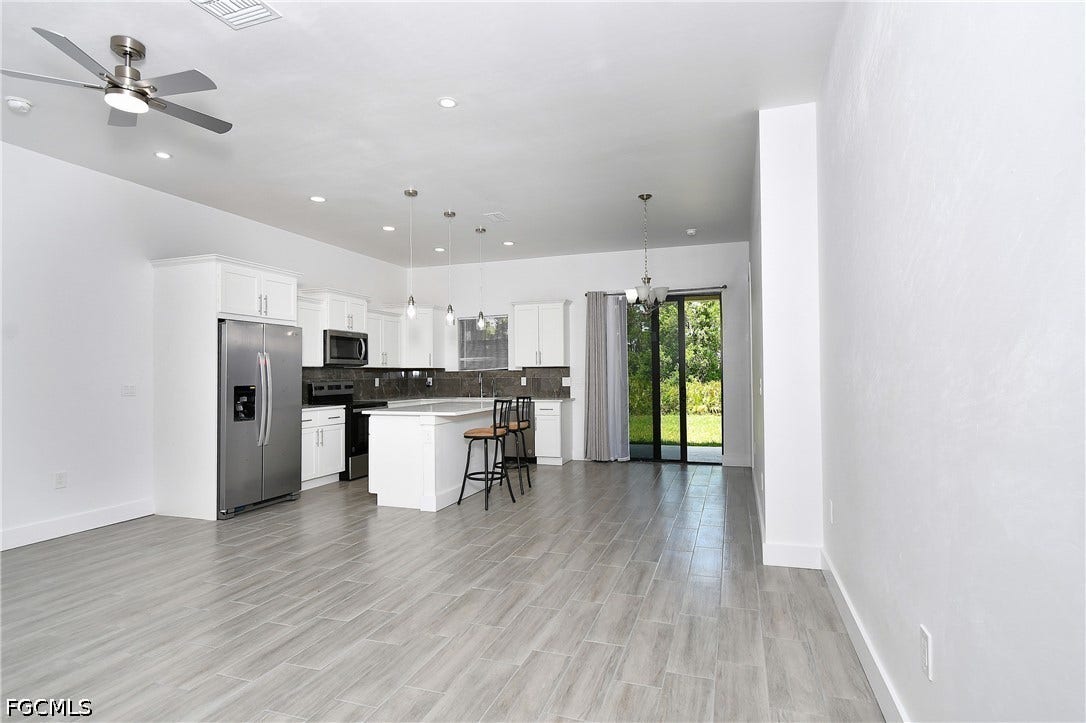 Kitchen with stainless steel appliances, a breakfast bar, white cabinetry, suspended lighting, and a kitchen island