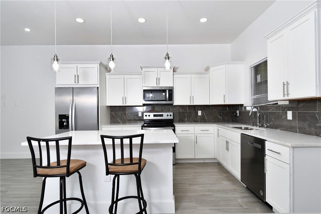 Kitchen with stainless steel appliances, pendant lighting, white cabinetry, and light wood-style floors