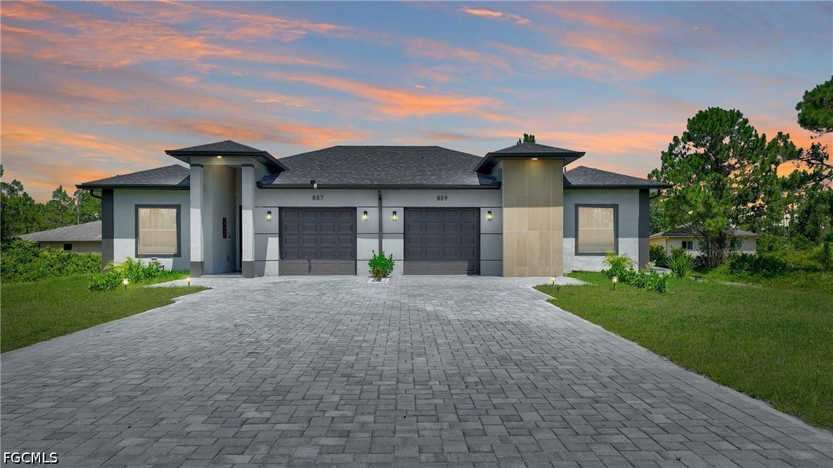 Prairie-style house featuring a front lawn, stucco siding, decorative driveway, and a garage