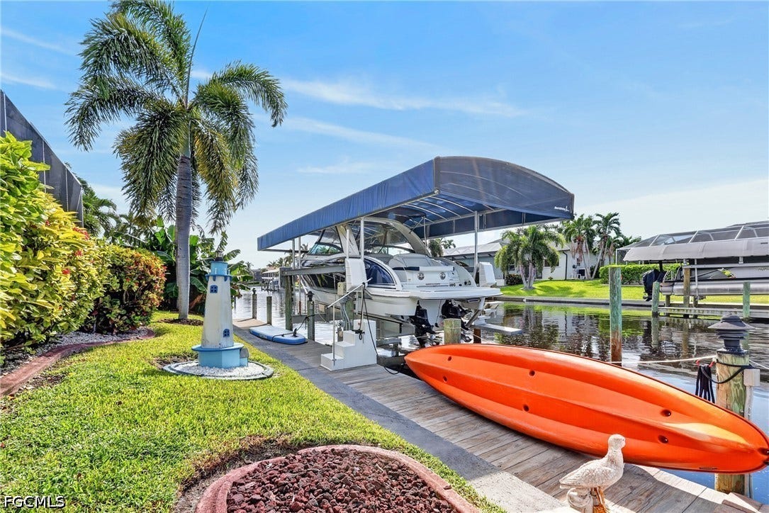 1416 SW 49th Terrace, Cape Coral, FL 33914 Waterfront access featuring a boat lift with canopy, extensive dockage, and lush landscaping