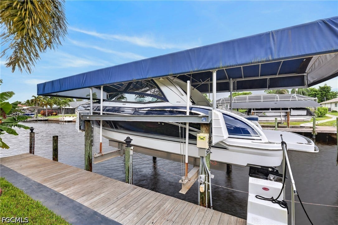 1416 SW 49th Terrace, Cape Coral, FL 33914 Waterfront property featuring a private boat lift with a blue canopy, wood dock, and canal access