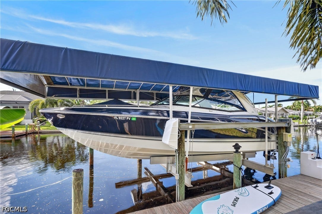 1416 SW 49th Terrace, Cape Coral, FL 33914 Waterfront property featuring a private boat lift with an overhead canopy, a wood plank dock, and direct canal access