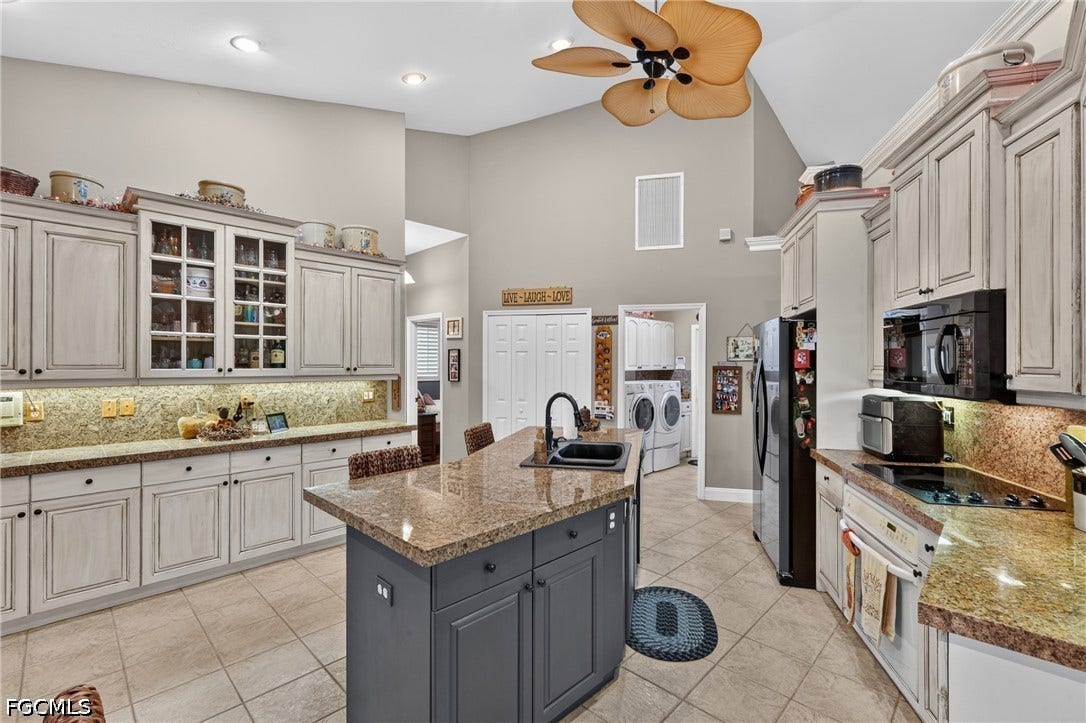 1416 SW 49th Terrace, Cape Coral, FL 33914 Kitchen featuring an island with a built-in sink, light-toned cabinetry, granite countertops, and tile flooring