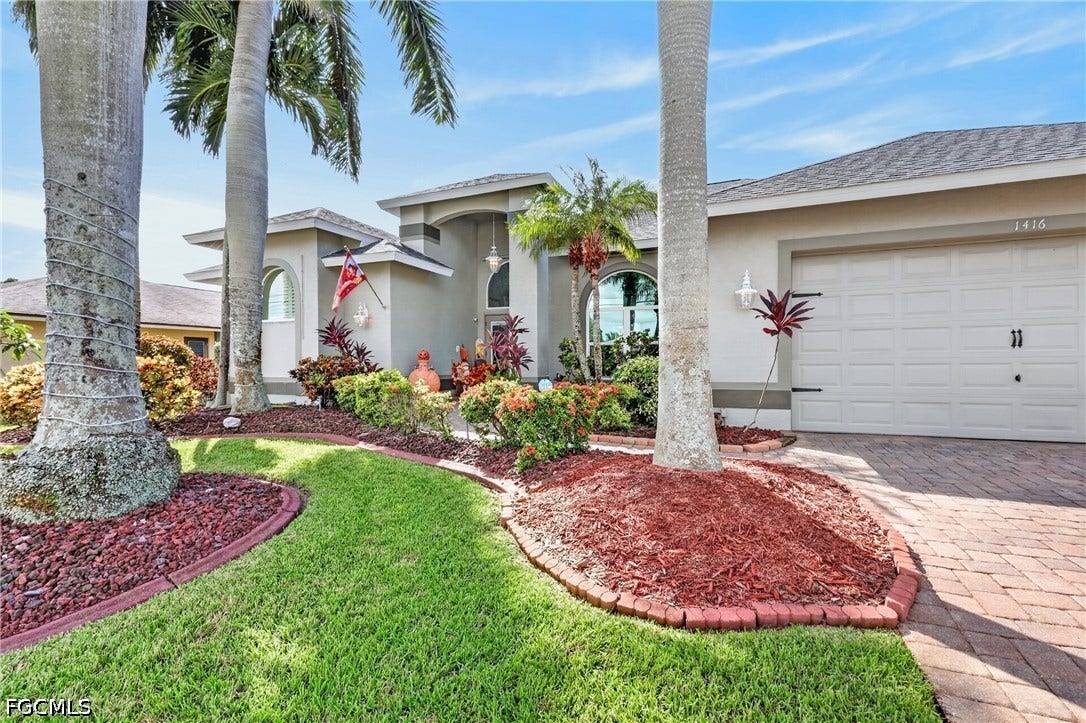 1416 SW 49th Terrace, Cape Coral, FL 33914 Stucco exterior with a shingled roof, arched window, and attached garage