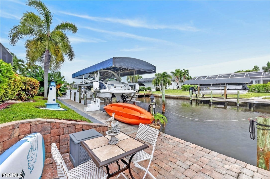 1416 SW 49th Terrace, Cape Coral, FL 33914 Waterfront property featuring a paver patio, stone retaining wall, private boat lift with canopy, and direct canal access
