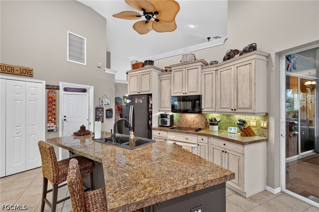 1416 SW 49th Terrace, Cape Coral, FL 33914 Kitchen featuring an island with a built-in sink, granite countertops, light wood-finish cabinetry, and a black microwave