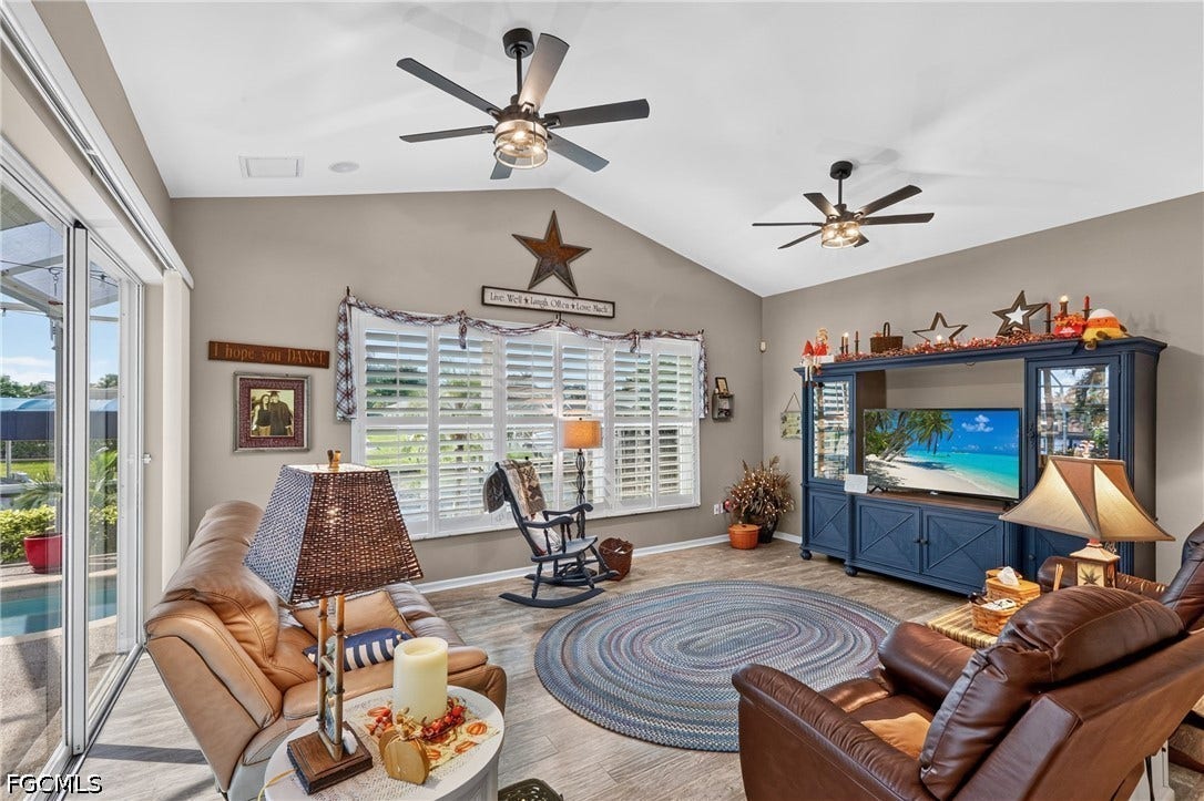 1416 SW 49th Terrace, Cape Coral, FL 33914 Vaulted ceiling living area featuring wood-finish flooring, two ceiling fans, and sliding glass doors leading to an outdoor pool area