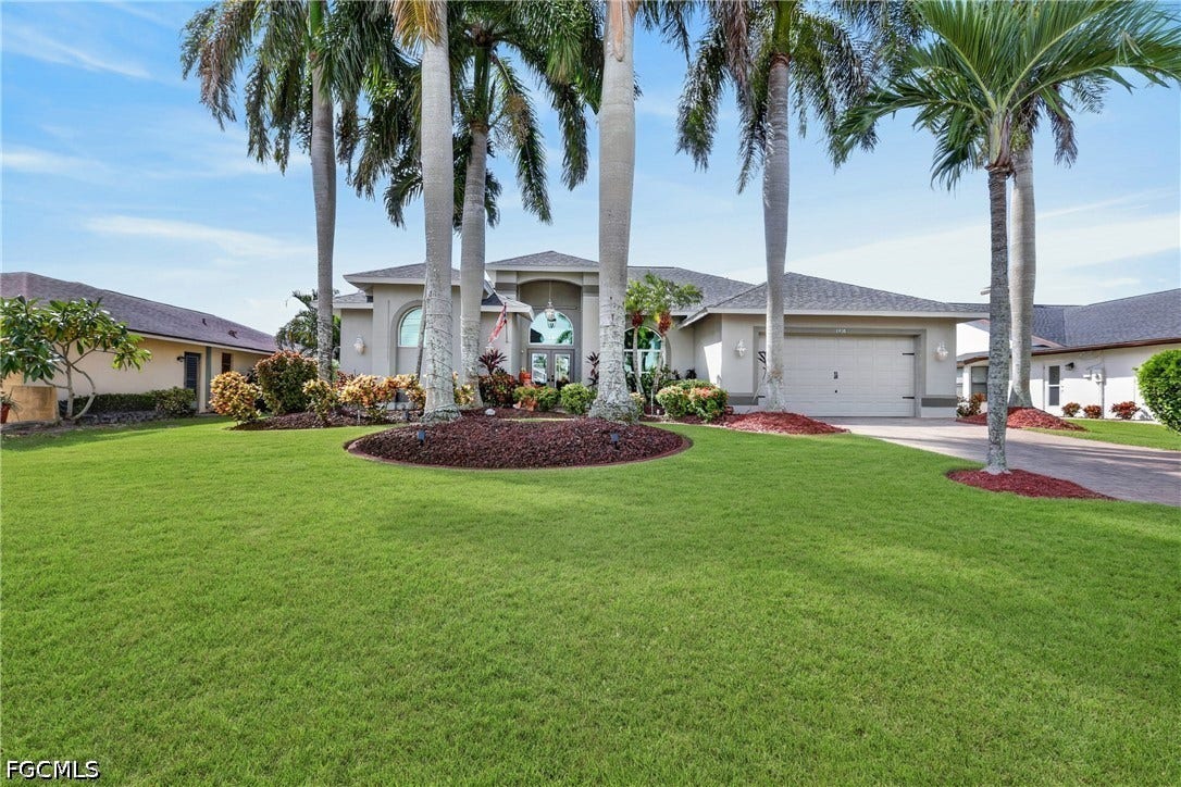 1416 SW 49th Terrace, Cape Coral, FL 33914 Expansive lawn with mature palm trees, a concrete driveway, and an attached garage