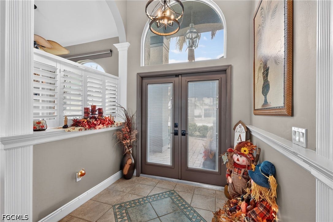 1416 SW 49th Terrace, Cape Coral, FL 33914 Interior arched transom window, double-door entry, decorative overhead lighting, wall paneling, and tile flooring