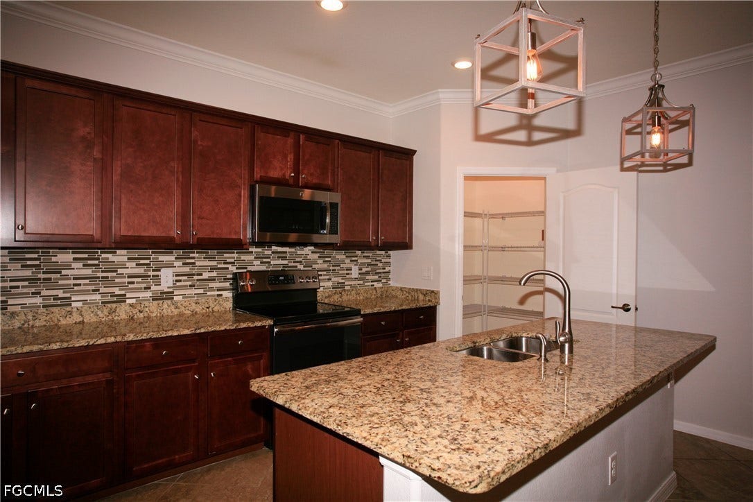 14495 Vindel Circle, Fort Myers, FL 33905 Kitchen featuring wood-finish cabinetry, granite countertops, a mosaic tile backsplash, stainless steel appliances, and an island with a double basin sink