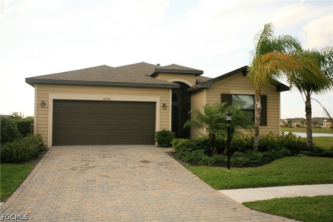 14495 Vindel Circle, Fort Myers, FL 33905 Beige exterior with a dark garage door, paved driveway, and mature landscaping