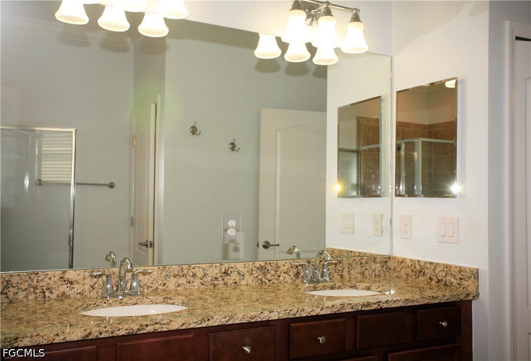 14495 Vindel Circle, Fort Myers, FL 33905 Dual vanity with a stone countertop and integrated sinks, complemented by a large wall-mounted mirror