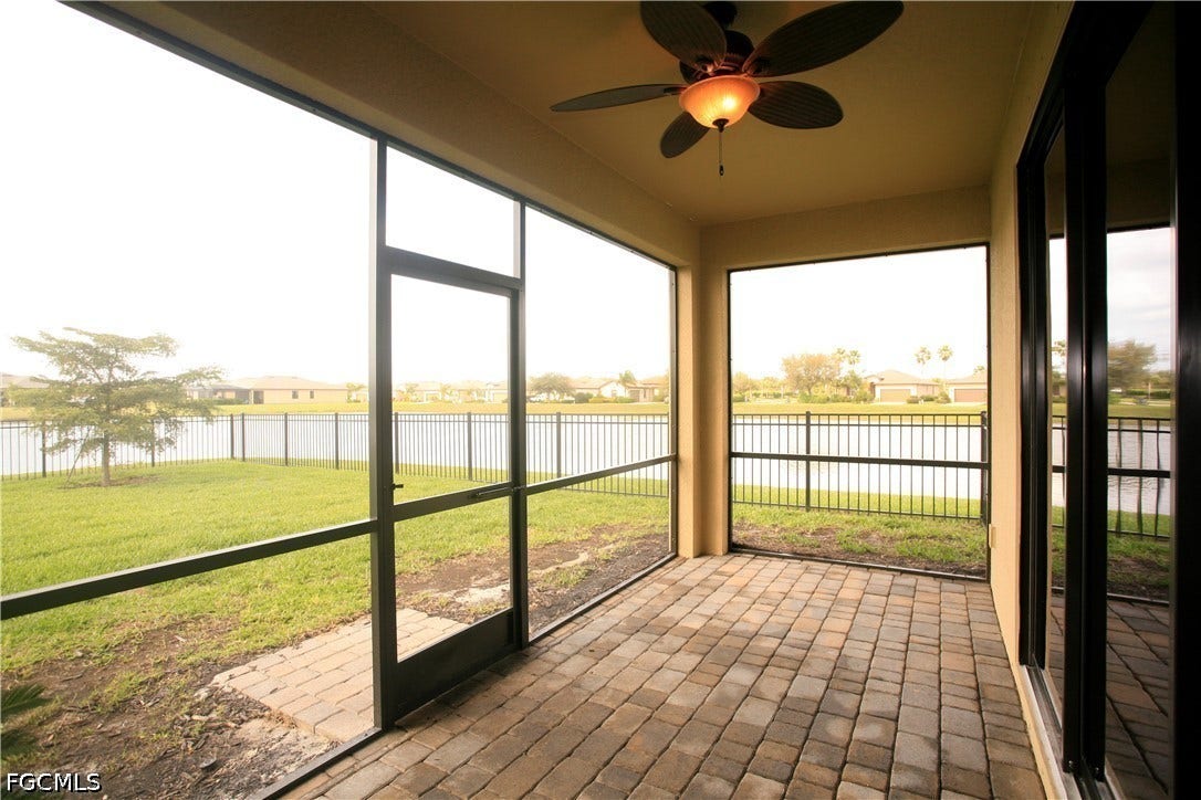14495 Vindel Circle, Fort Myers, FL 33905 Screened-in patio with paver flooring, overhead ceiling fan with light fixture, and a black wrought iron fence bordering a body of water