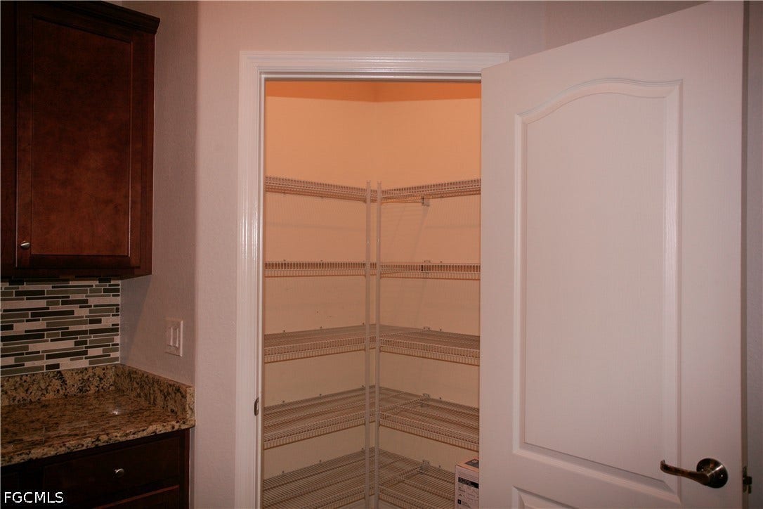 14495 Vindel Circle, Fort Myers, FL 33905 Corner pantry with multiple wire shelving units, a white paneled door, a granite-look countertop, and a mosaic tile backsplash