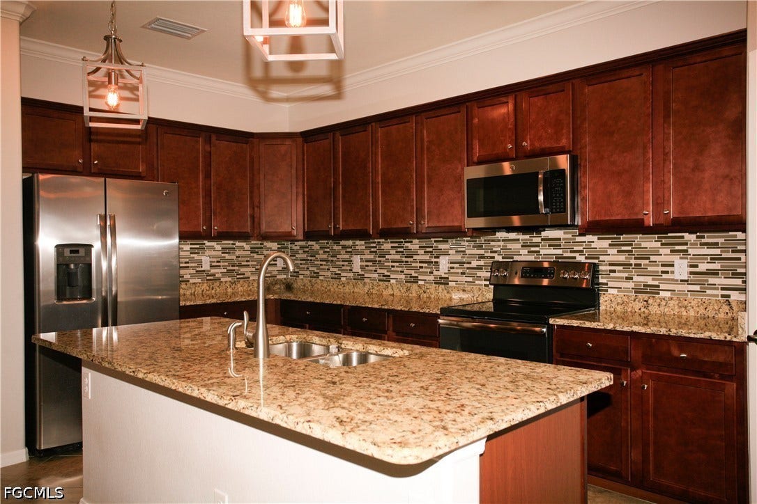 14495 Vindel Circle, Fort Myers, FL 33905 Kitchen featuring a central island with dual sinks, natural stone countertops, rich wood-finish cabinetry, and stainless steel appliances